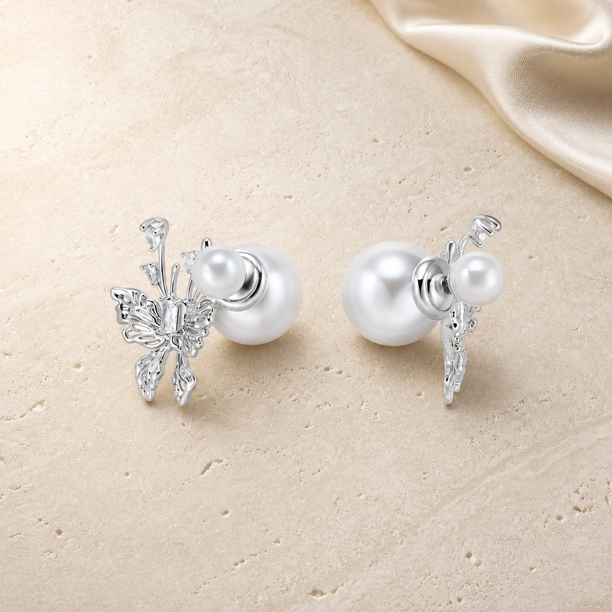 Silver butterfly double pearl stud earrings on ivory travertine