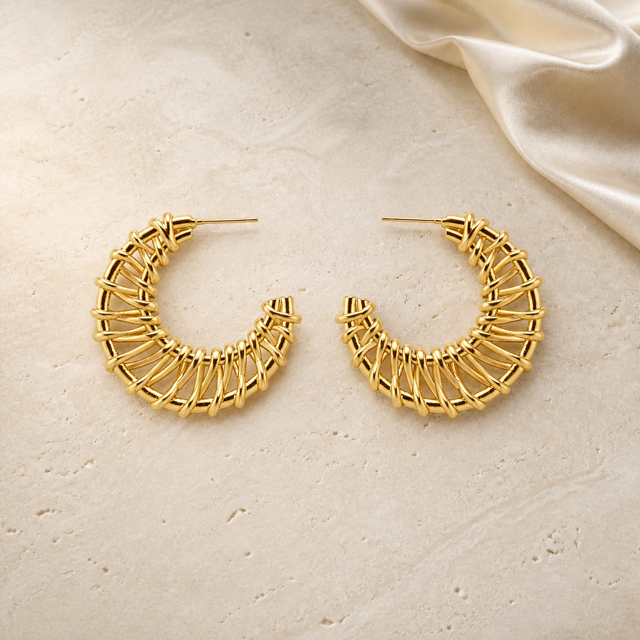 Gold hand-woven open hoop earrings on ivory travertine