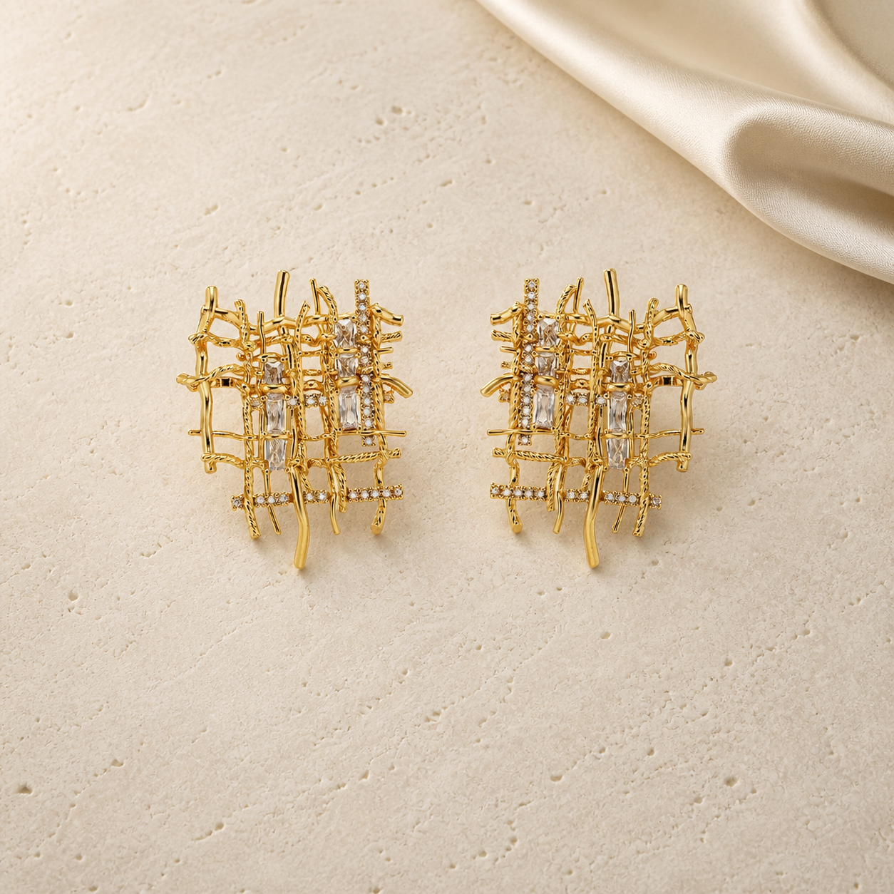 Gold handwoven asymmetric zircon stud earrings on ivory travertine
