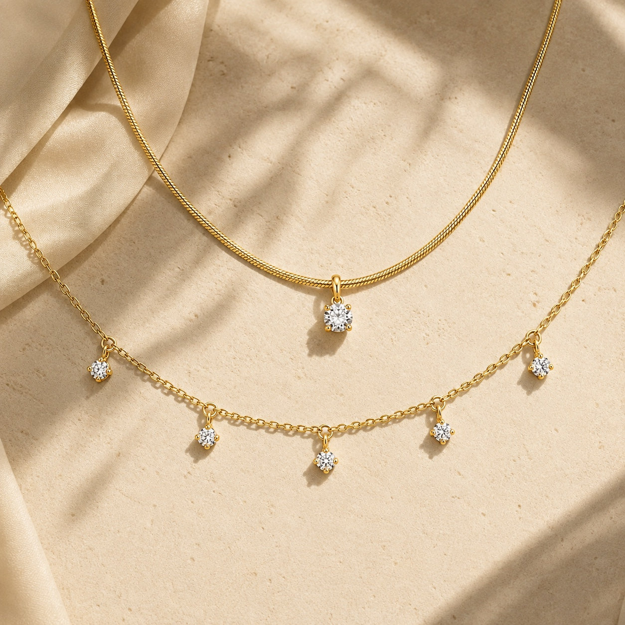 Aurelia Gold Solitaire and Five-Stone Necklace layered on warm stone with soft sunlight