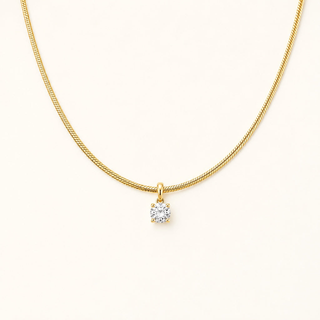 Aurelia Gold Solitaire Necklace with a single clear stone on an ivory background