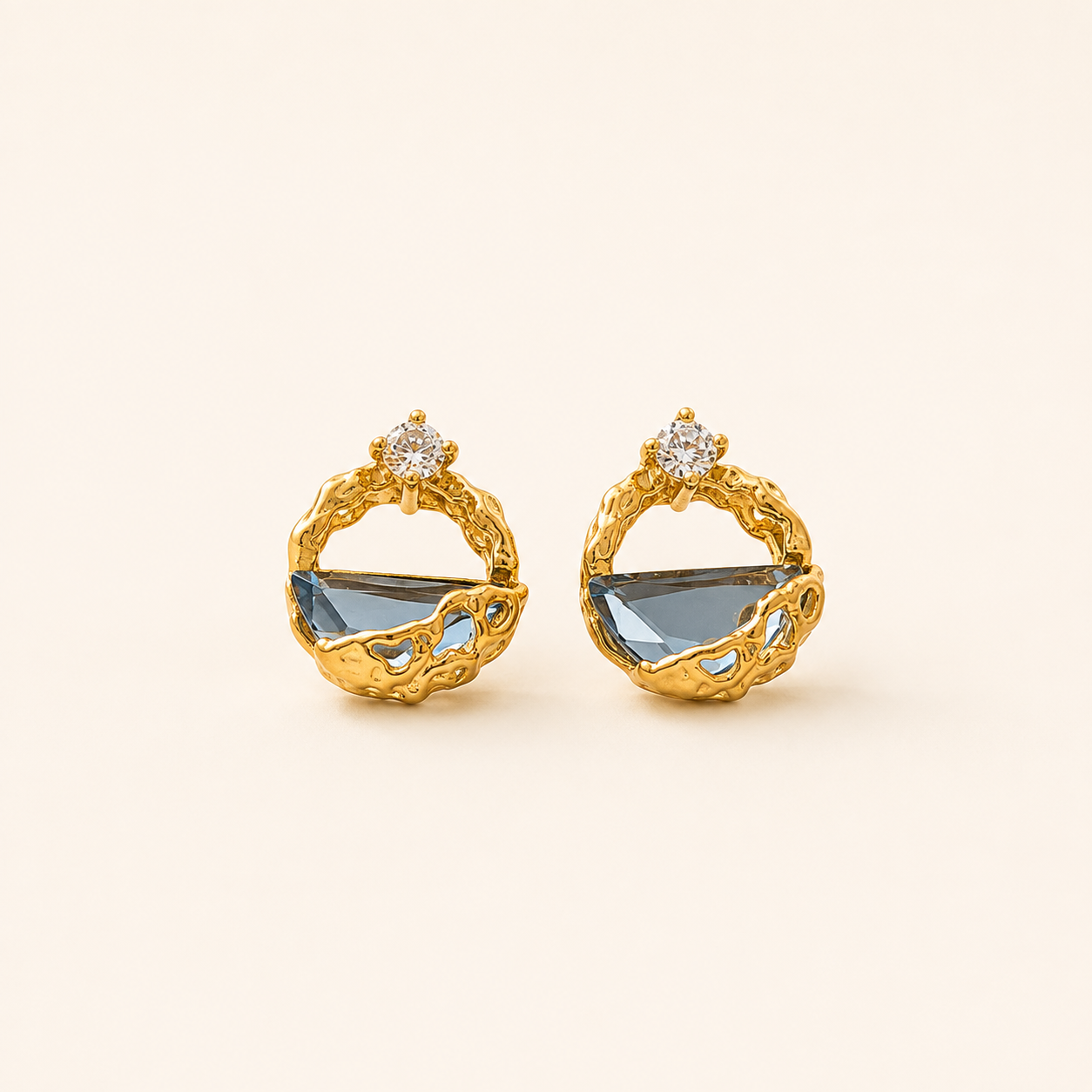 Pair of gold-tone Celeste earrings with blue glass imitation crystals on a clean cream background