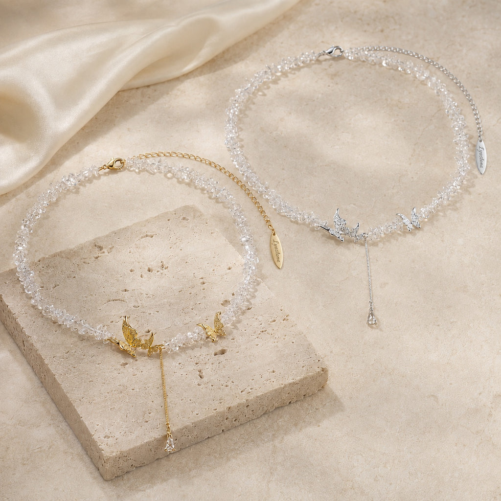 Gold and silver tone crystal butterfly necklaces styled on ivory travertine.