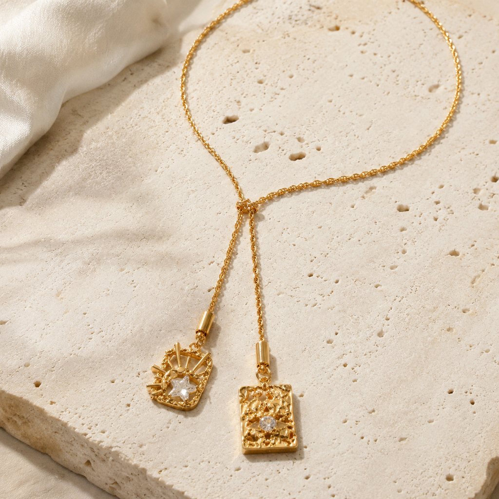 Celestial Duo Lariat Necklace styled on warm ivory travertine with two sculptural crystal pendants.
