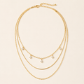 Gold-tone three-layer sterling silver necklace with five square crystals on warm ivory background
