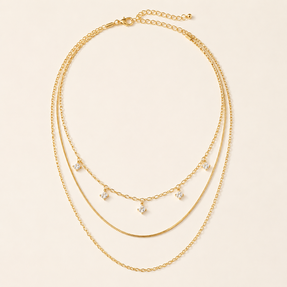 Gold-tone three-layer sterling silver necklace with five square crystals on warm ivory background