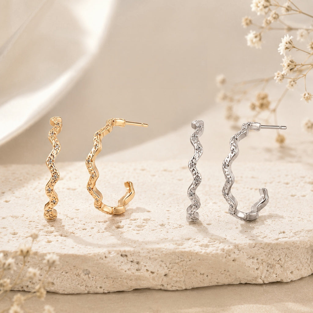 Lyastone gold and silver sculpted wavy hoop earrings on warm ivory stone
