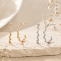 Lyastone gold and silver sculpted wavy hoop earrings on warm ivory stone