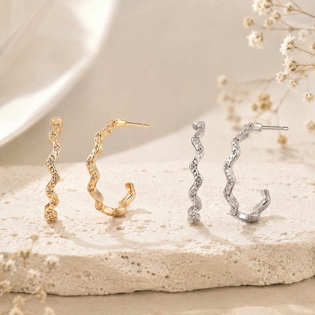 Lyastone gold and silver sculpted wavy hoop earrings on warm ivory stone
