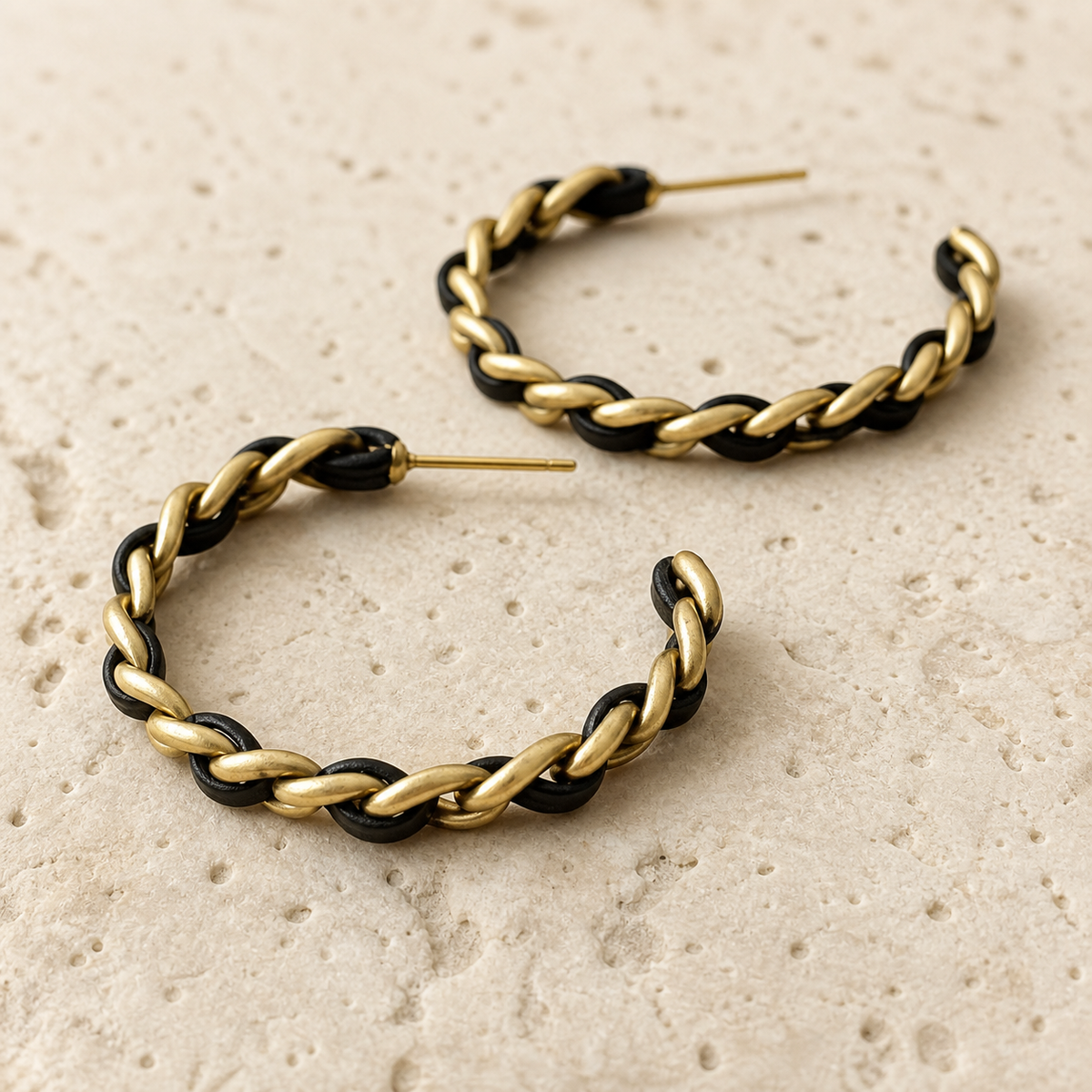 Close-up detail of black and gold-tone woven chain hoop earrings