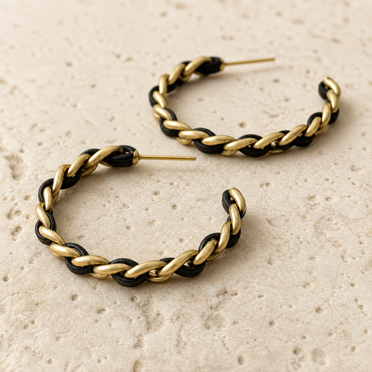 Close-up detail of black and gold-tone woven chain hoop earrings