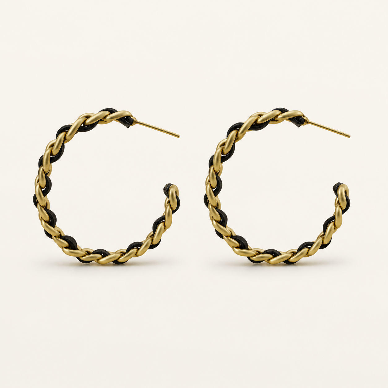 Noir Weave black and gold-tone open hoop earrings on a warm neutral background