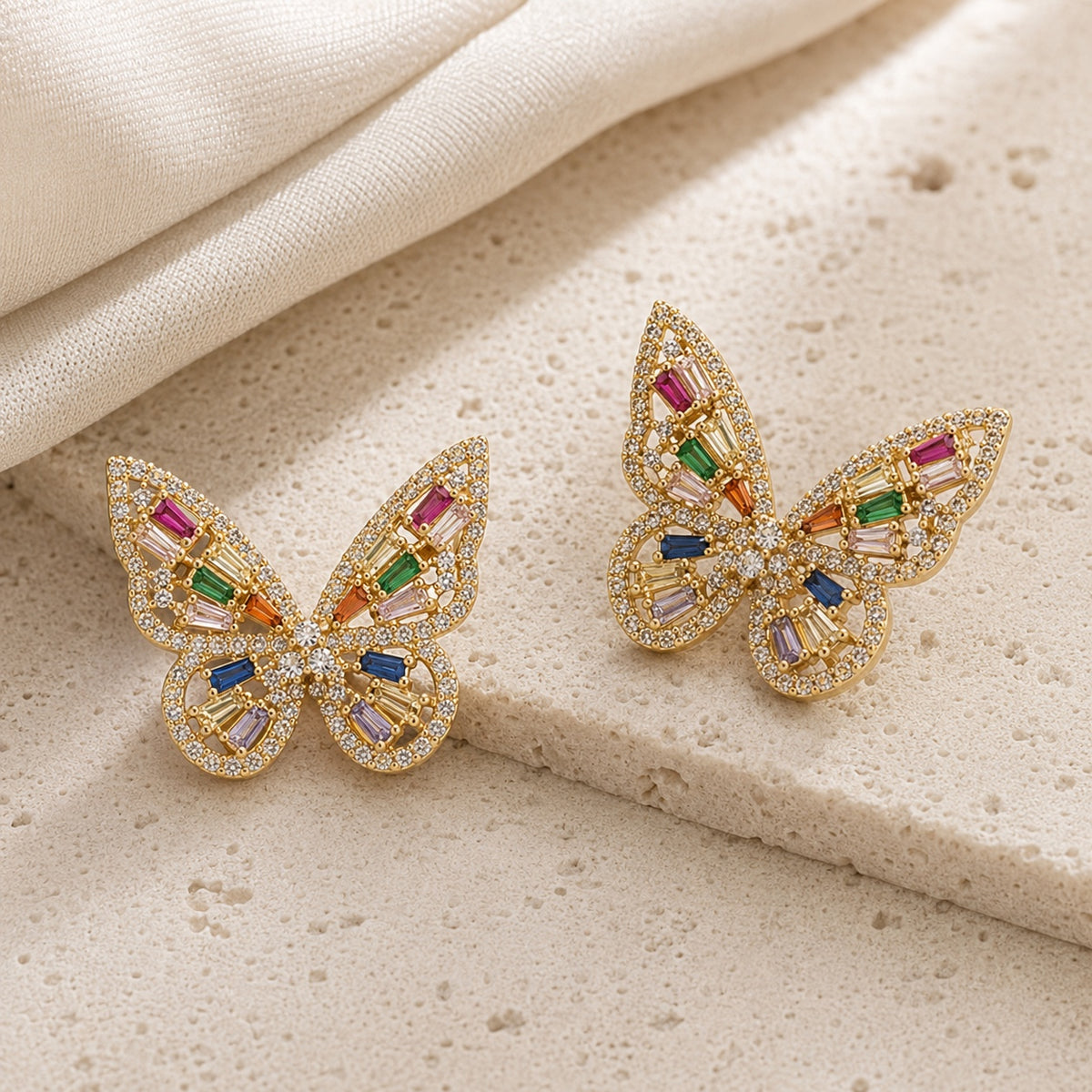 Prism Flutter Butterfly Earrings in gold tone with multicolour cubic zirconia on warm travertine